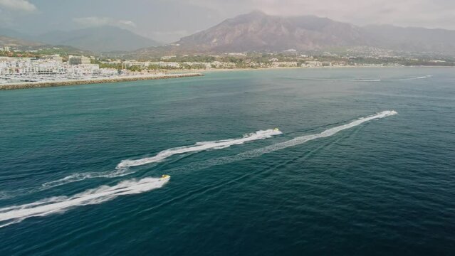 Jet skis racing near puerto banus in marbella with scenic mountains, aerial view