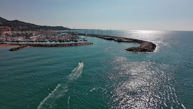 A lone skate surfer cruising near port ginesta in barcelona, spain, glimmering sea under the sun, aerial view