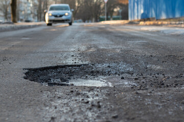 A pothole in the road and a car in the background that is moving towards this pothole