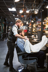 Fancy hairdresser putting on a cape on customer. Professional barber preparing everything for appointment. Confident man visiting barbershop.