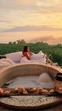 bathtub looking out over the mountains of Northern Thailand during vacation. Outdoor bathroom during sunrise with fog and mist, Asian woman drinking coffee on the balcony in the morning in outdoor ebd