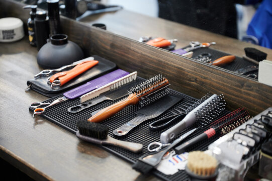 Close up view of hairdresser's tools. Cropped photo of barber's equipment on wooden table. Different combs and brushes lying on background of mirror.