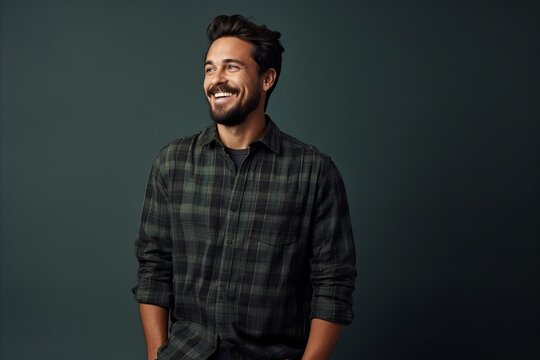 Handsome young bearded man in checkered shirt smiling and looking at camera.