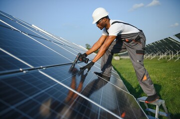African american man in safety helmet and glasses tighten nuts on solar panels with screwdriver. Competent technician using tools while performing service work on station