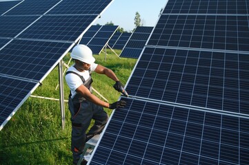 African American engineer maintaining solar cell panels. Technician working outdoor on ecological solar farm construction. Renewable clean energy technology concept