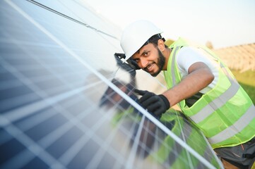 Male arab engineer standing on field with rows of solar panels.