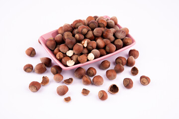 brown hazelnuts in pink bowl. nuts inside and outside the bowl on a white background