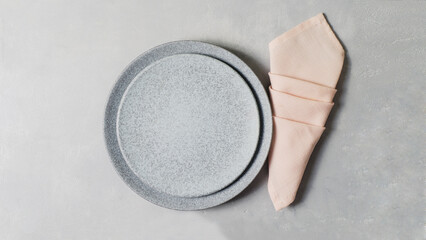 Table setting. Two marble effect dinner plates on grey concrete table with pink folded napkin