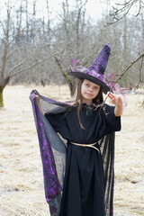 Teenage girl in purple witch costume in gray empty garden in autumn.