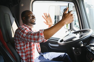 African driver in the cabin of a truck talking on the phone.