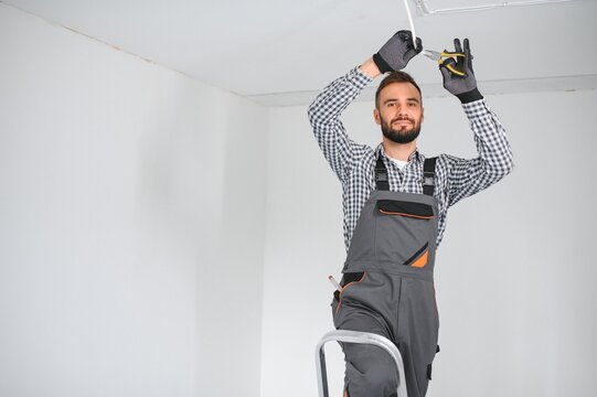 Young electrician installing smoke detector on ceiling.