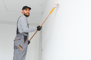 Young worker painting wall in room.