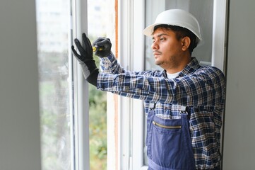 Indian Workman in overalls installing or adjusting plastic windows in the living room at home