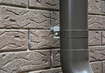 Close up on house rain gutter downspout pipe anchor bolt holder on the brick wall.