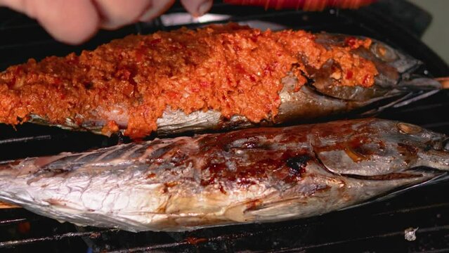 Asian woman's hands apply spicy spices to grilled skipjack tuna (Katsuwonus pelamis). This food is a typical seafood dish from East Java, Indonesia