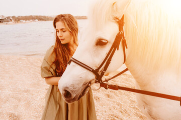 A woman in a dress stands next to a white horse on a beach, with the blue sky and sea in the...