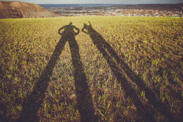 Two People Are Standing In A Field With Their Shadows On The Grass