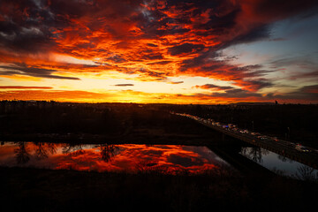 A magical sunset in Krakow, Nowa Huta bridge, Wisła River, viaduct, traffic jam, enchanting clouds tinted with red, drone view, aerial photo, urban transportation challenge - obrazy, fototapety, plakaty