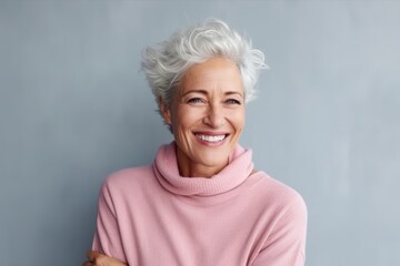 Portrait of a happy senior woman standing with arms crossed against grey background