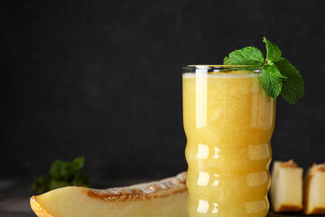 Glass of tasty melon smoothie with mint on black background