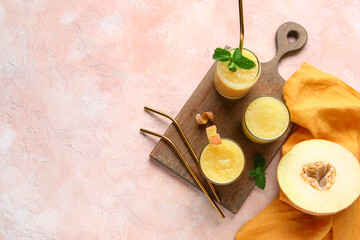 Wooden board with glasses of tasty melon smoothie and mint on pink background