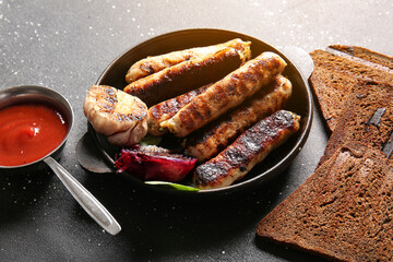 Frying pan of tasty grilled sausages, sauce and bread on black background