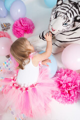 A little girl is feeding a white realistic stuffed toy tiger. Birthday party celebration.
