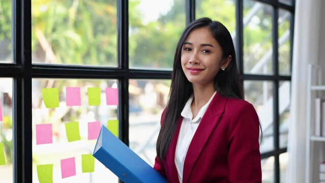 An attractive Asian woman in a red suit standing holding a work file Financial document files in the meeting internal presentation Company management concept.