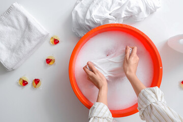 Woman washing laundry in basin with water on white table, top view