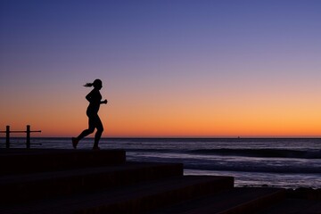 silhouette of person jogging on beach steps at dawn