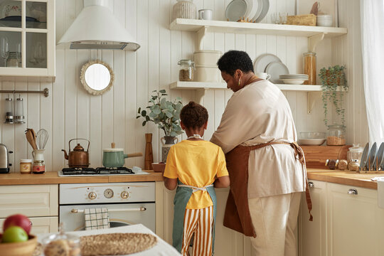 Rear view of African American granny and granddaughter wearing aprons cooking meal in cozy kitchen, copy space