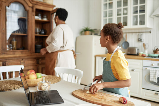 Selective focus shot of African American grandma and granddaughter spending time together cooking meal in kitchen