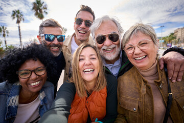 Group of diverse cheerful middle-aged tourist friends posing smiling taking a photo selfie embracing together with front camera on travel outdoor. Mature happy six people enjoy holidays sunny day  - obrazy, fototapety, plakaty