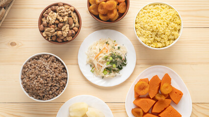 table with boiled healthy food, boiled vegetables, nuts, boiled buckwheat, dried apricots, sauerkraut, top view. wooden table