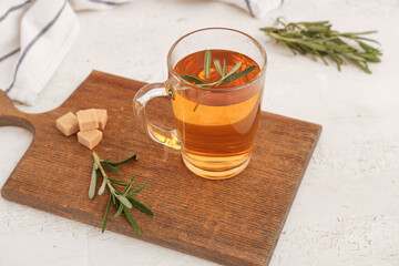 Wooden board with glass cup of hot rosemary tea and sugar on white background