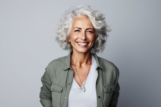Smiling senior woman with grey hair. Attractive mature woman looking at camera and smiling while standing against grey background