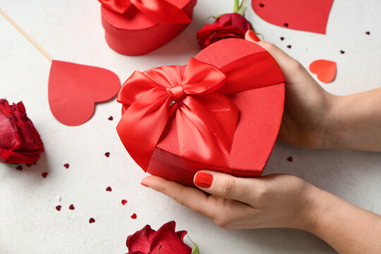 Female hands with red manicure, gift box and decor on white grunge background. Valentine's Day celebration