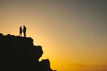 silhouettes of pair standing on cliff, sunrise in background