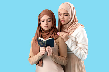 Fototapeta premium Young Muslim women in hijab with Koran on blue background