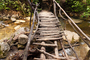 Wooden flooring of a dilapidated bridge over a mountain river on an ecological trail in a summer mountain forest.