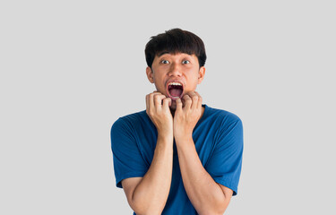 Young Asian man in blue t-shirt having a big surprise, isolated on gray background. The concept of...