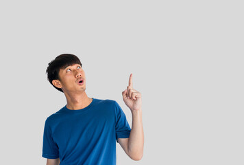 Shocked face of Asian man in blue shirt isolated on gray background. Person's index finger pointing...