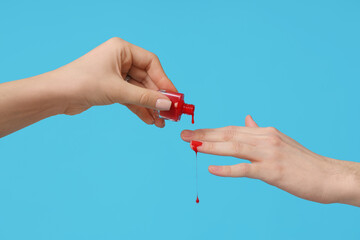 Female hands with bottle of dripping red nail polish on blue background