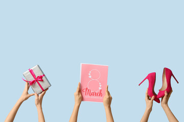 Female hands with festive postcard, gift box and high heel shoes on blue background. International...