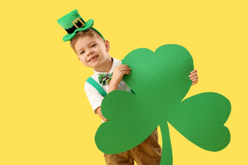 Cute little boy with leprechaun's hat and paper clover leaf on yellow background. St. Patrick's Day...