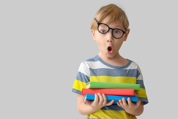 Surprised little boy in eyeglasses with books near grey wall