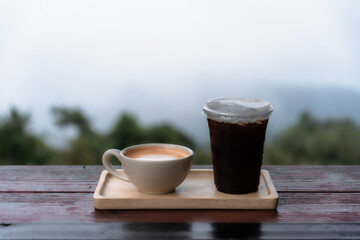 Americano iced coffee or black coffee and Hot milk tea in cup on wood desk with Foggy forest Beautiful landscape Scenic view of misty mountain nature background.