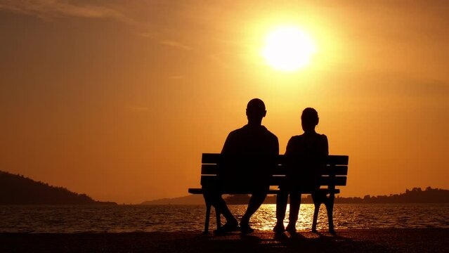 Couple silhouette on bench enjoy evening. A man and woman silhouettes sitting together and enjoy the nightfall sky by the lake.