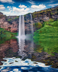 Seljalandsfoss watterfall reflected in the calm waters of river. Green mormimg scene of Iceland, Europe. Beauty of nature concept background.