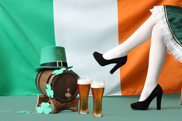 Woman in waitress costume with glasses of beer, barrel and Irish flag on green background. St....